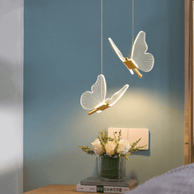 Load image into Gallery viewer, Two gold LED Butterfly Pendant Lights above bedside table next to bed in bedroom
