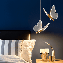 Load image into Gallery viewer, Two gold LED Butterfly Pendant Lights above bedside table in bedroom
